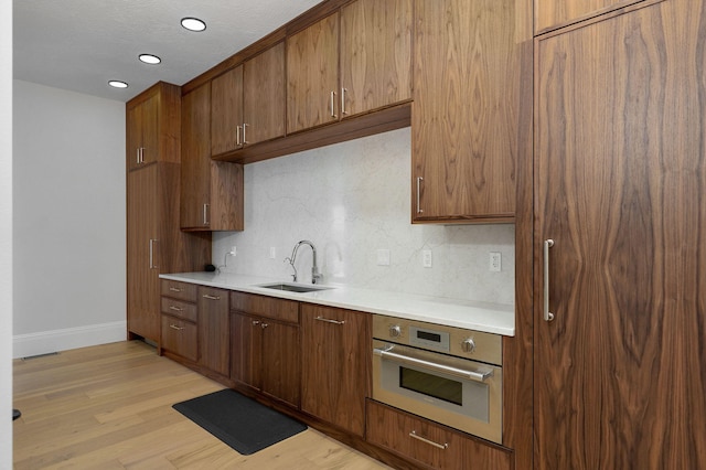 kitchen featuring light wood-style flooring, a sink, decorative backsplash, light countertops, and stainless steel oven