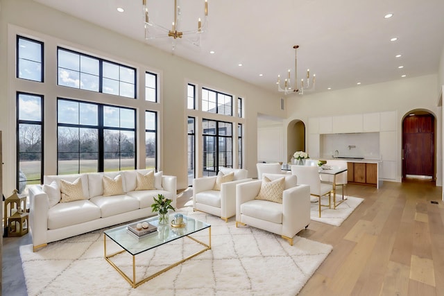 living area with an inviting chandelier, recessed lighting, light wood-style floors, and arched walkways