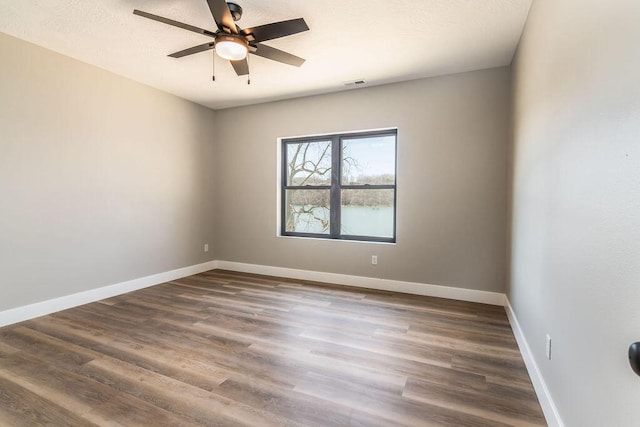 empty room with visible vents, a textured ceiling, dark wood finished floors, baseboards, and ceiling fan