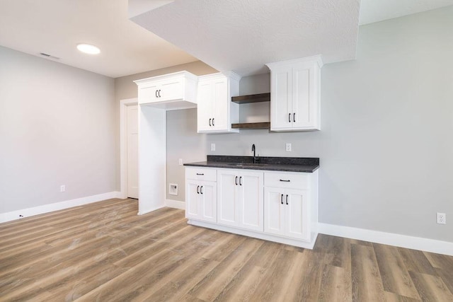 kitchen featuring open shelves, light wood-style flooring, a sink, white cabinets, and dark countertops