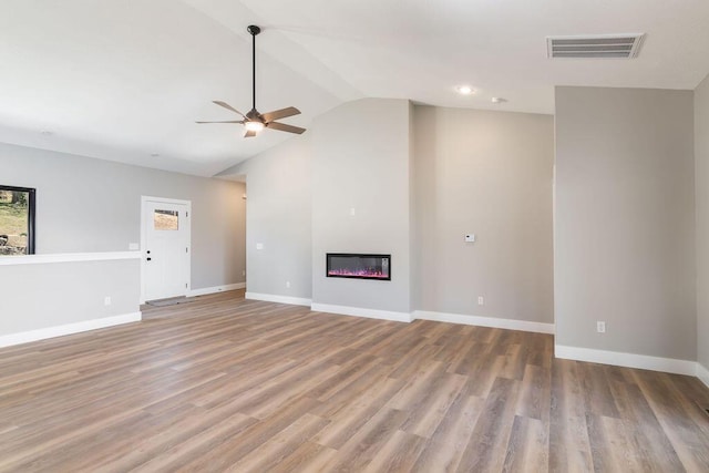 unfurnished living room featuring visible vents, baseboards, vaulted ceiling, wood finished floors, and a glass covered fireplace