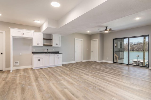 kitchen with dark countertops, baseboards, open floor plan, light wood-type flooring, and white cabinetry