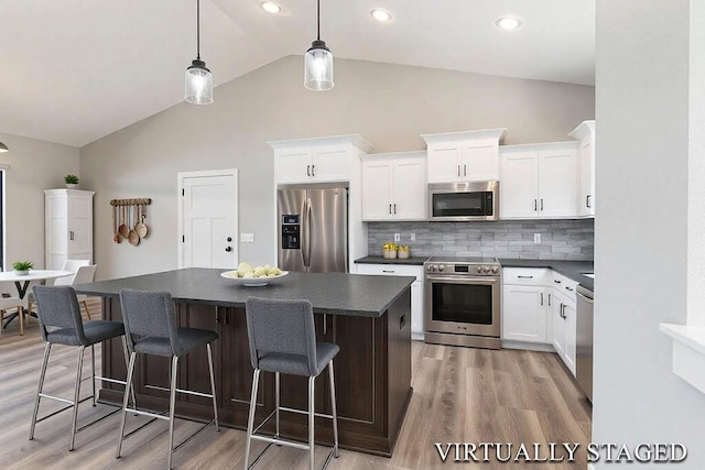 kitchen with light wood-style floors, stainless steel appliances, a kitchen island, and dark countertops