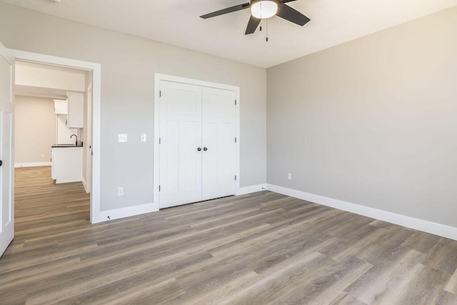 unfurnished bedroom featuring ceiling fan, a closet, baseboards, and wood finished floors