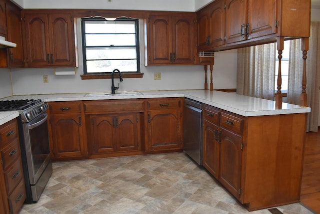 kitchen with light countertops, a peninsula, brown cabinetry, stainless steel appliances, and a sink