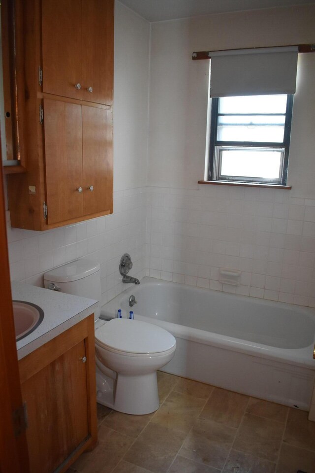 full bathroom with vanity, tile walls, toilet, and a tub