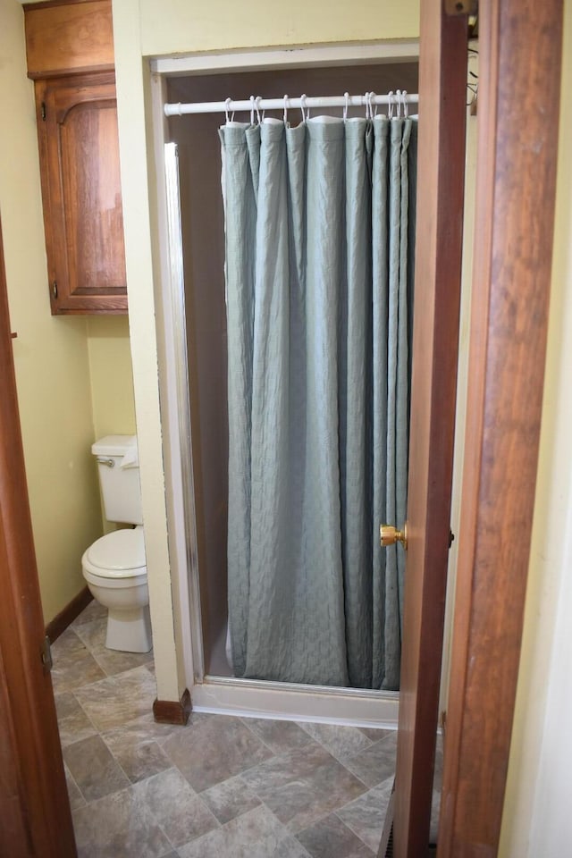 full bath featuring a shower stall, stone finish floor, toilet, and baseboards