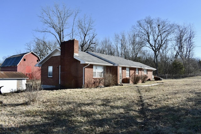 view of side of home featuring brick siding, a barn, a lawn, a chimney, and an outdoor structure