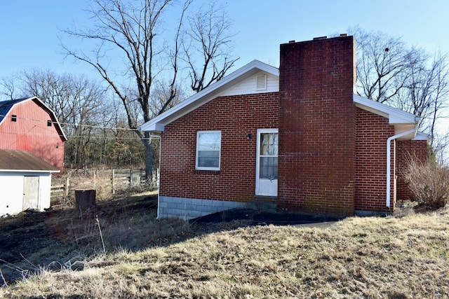 view of side of property with brick siding, a barn, a chimney, and an outdoor structure