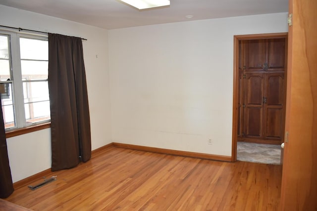 unfurnished room featuring visible vents, light wood-style floors, and baseboards