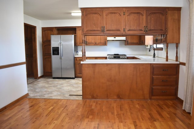 kitchen with under cabinet range hood, a sink, appliances with stainless steel finishes, a peninsula, and light countertops