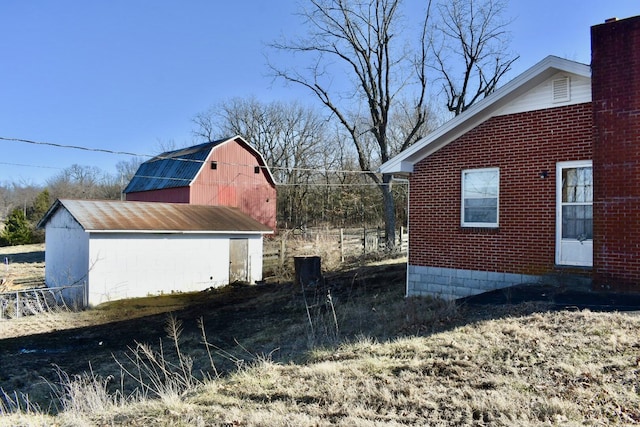 view of side of property with an outbuilding, a gambrel roof, a chimney, a barn, and brick siding