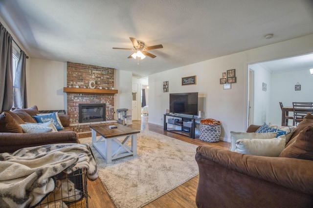 living room with a ceiling fan, wood finished floors, baseboards, a textured ceiling, and a brick fireplace