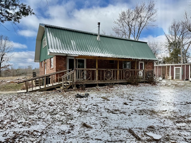 view of front of home featuring metal roof, a gambrel roof, brick siding, and covered porch