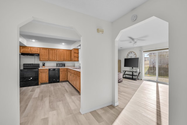 kitchen featuring black appliances, a sink, under cabinet range hood, light wood finished floors, and light countertops