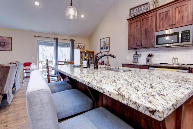 kitchen with stainless steel microwave, backsplash, light wood-type flooring, lofted ceiling, and a sink