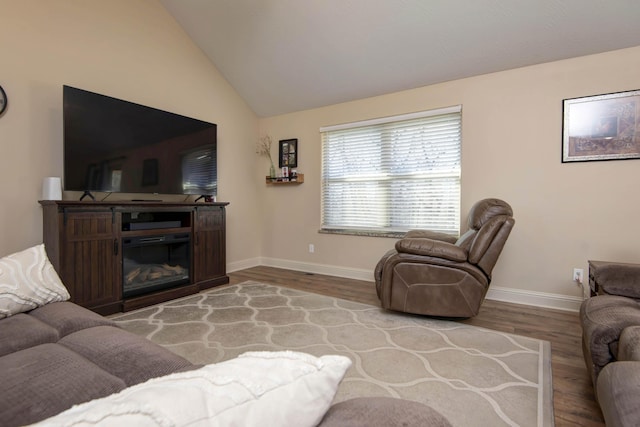 living room with a glass covered fireplace, vaulted ceiling, wood finished floors, and baseboards