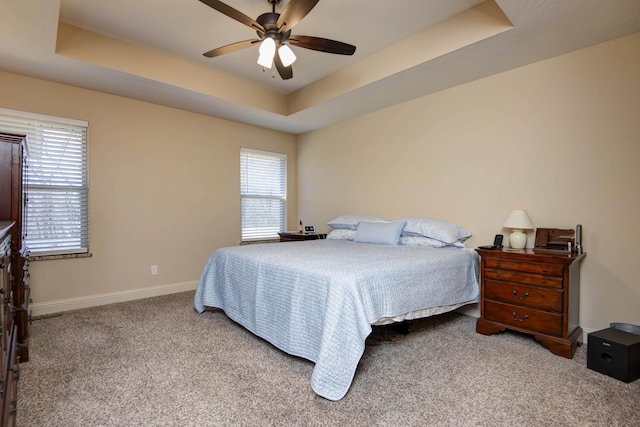 carpeted bedroom with a tray ceiling, a ceiling fan, and baseboards