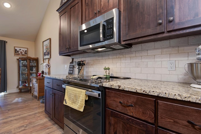 kitchen featuring backsplash, light stone countertops, lofted ceiling, appliances with stainless steel finishes, and light wood-style floors