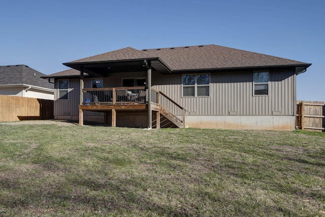 rear view of house featuring fence, a wooden deck, stairs, roof with shingles, and a lawn