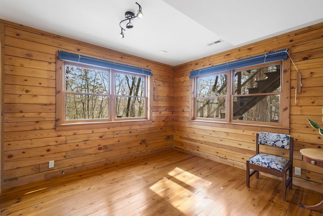 unfurnished room with light wood-style flooring, visible vents, and wood walls