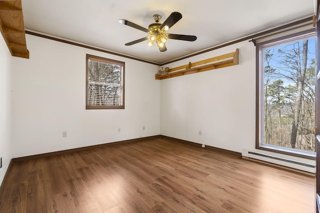 empty room featuring baseboard heating, a healthy amount of sunlight, wood finished floors, and ornamental molding