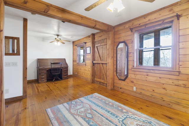 unfurnished office featuring wood walls, baseboards, a ceiling fan, and wood-type flooring