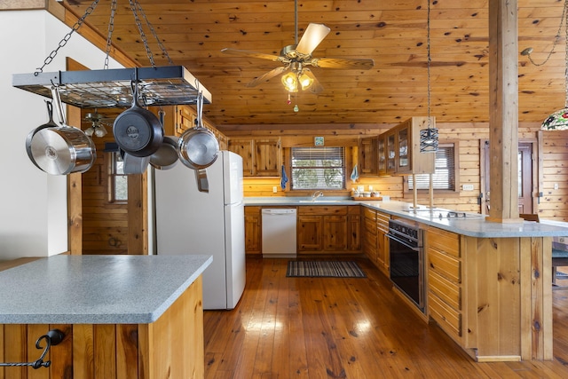 kitchen with a peninsula, hardwood / wood-style flooring, brown cabinetry, white appliances, and a sink