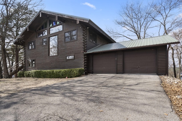 view of side of home with log siding, metal roof, an attached garage, and aphalt driveway