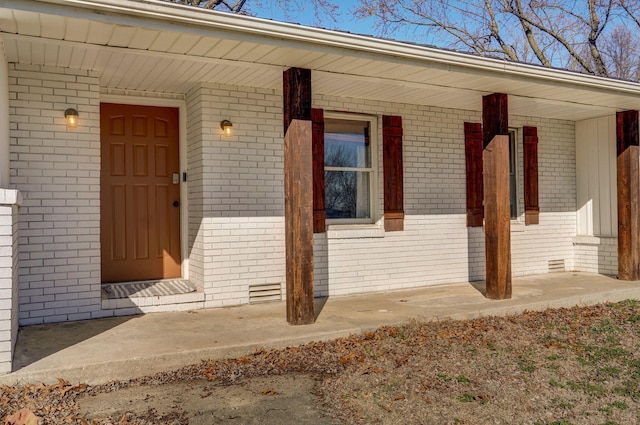 entrance to property with crawl space, brick siding, and covered porch