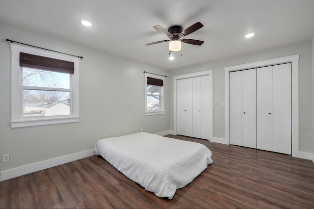 bedroom featuring dark wood-style floors, multiple windows, baseboards, and multiple closets