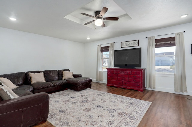 living room featuring wood finished floors, baseboards, a tray ceiling, recessed lighting, and ceiling fan