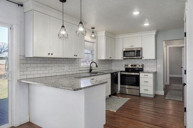 kitchen with a peninsula, dark wood-type flooring, appliances with stainless steel finishes, white cabinetry, and tasteful backsplash