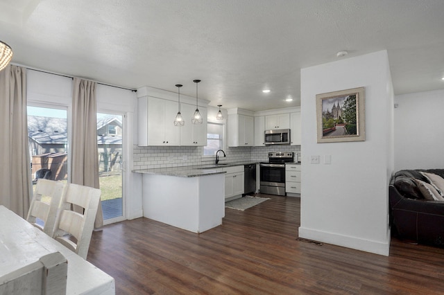 kitchen with dark wood-style flooring, stainless steel appliances, white cabinets, decorative light fixtures, and tasteful backsplash