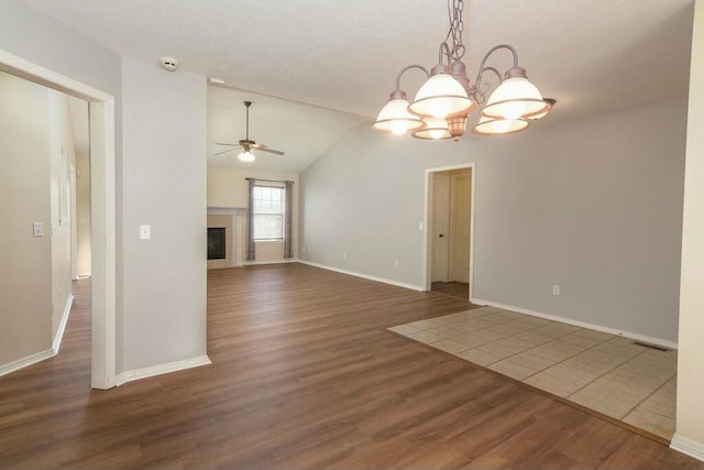 175 Mesquite Dr, Branson, MO 65616 - unfurnished living room featuring a tiled fireplace, vaulted ceiling, ceiling fan with notable chandelier, wood finished floors, and a textured ceiling