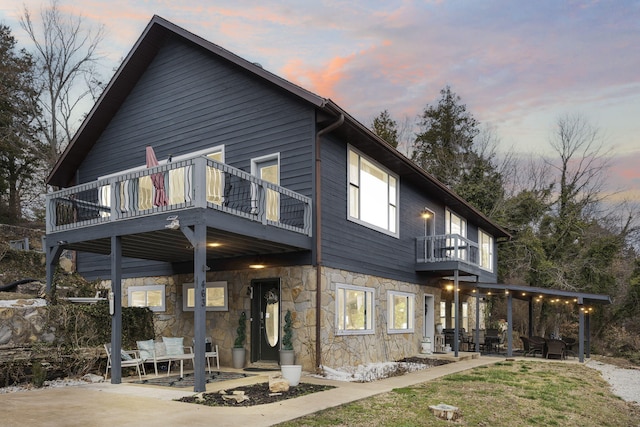 back of house at dusk with a patio and a balcony