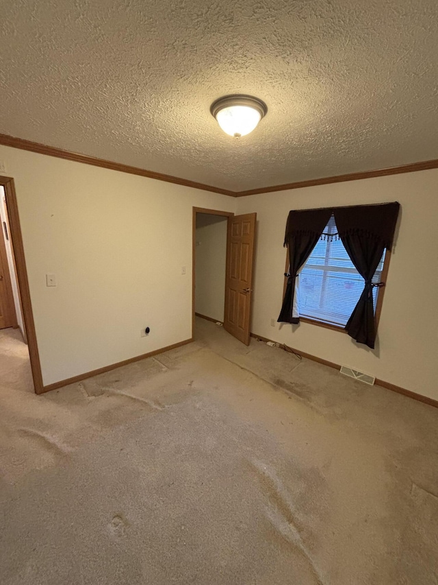 spare room with a textured ceiling, light carpet, visible vents, and ornamental molding