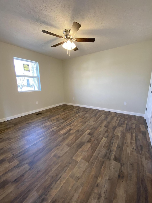 spare room featuring a textured ceiling, dark wood-type flooring, and baseboards