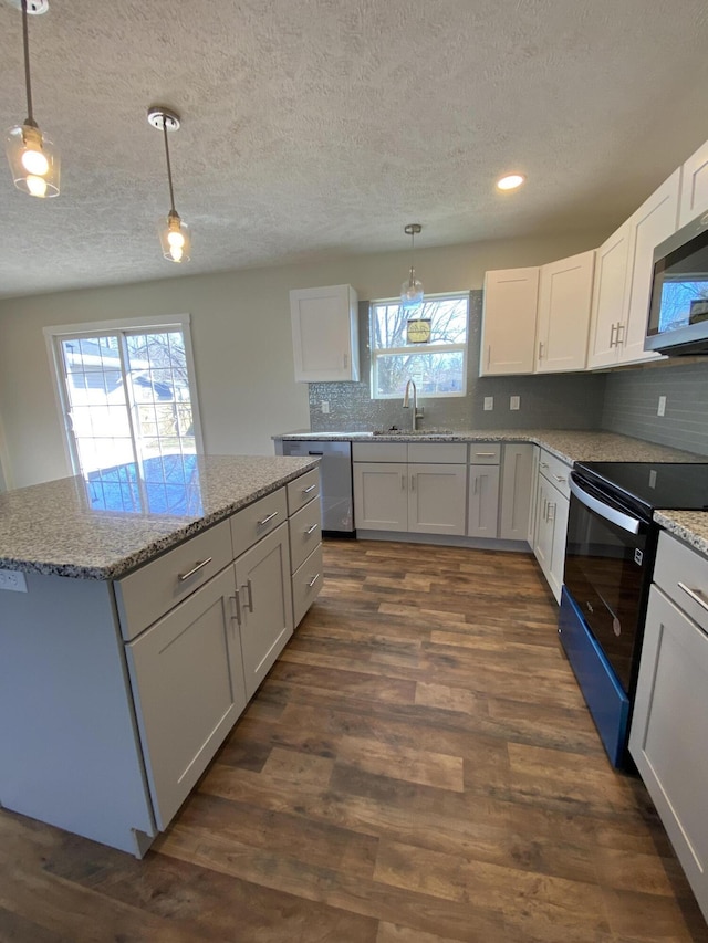 kitchen with a sink, light stone counters, appliances with stainless steel finishes, decorative backsplash, and dark wood-style flooring