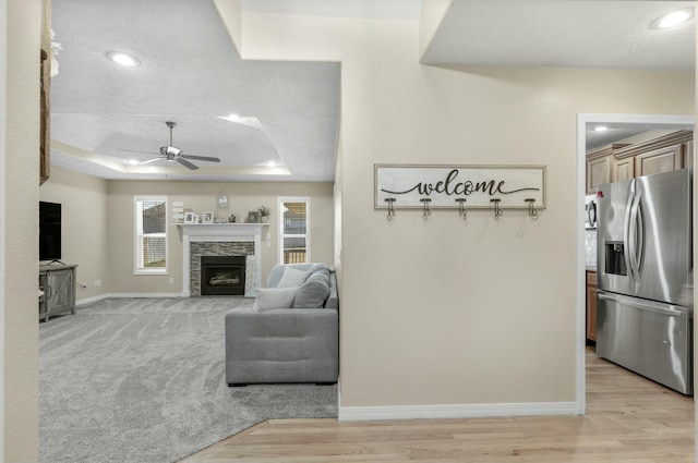 living area with light wood finished floors, baseboards, ceiling fan, a fireplace, and a raised ceiling