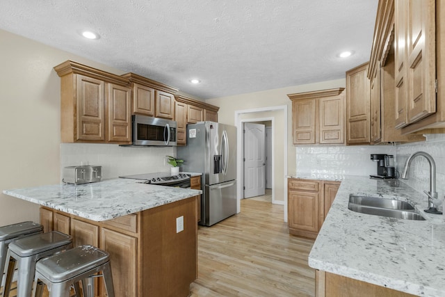 kitchen featuring light wood finished floors, a breakfast bar area, appliances with stainless steel finishes, a peninsula, and a sink