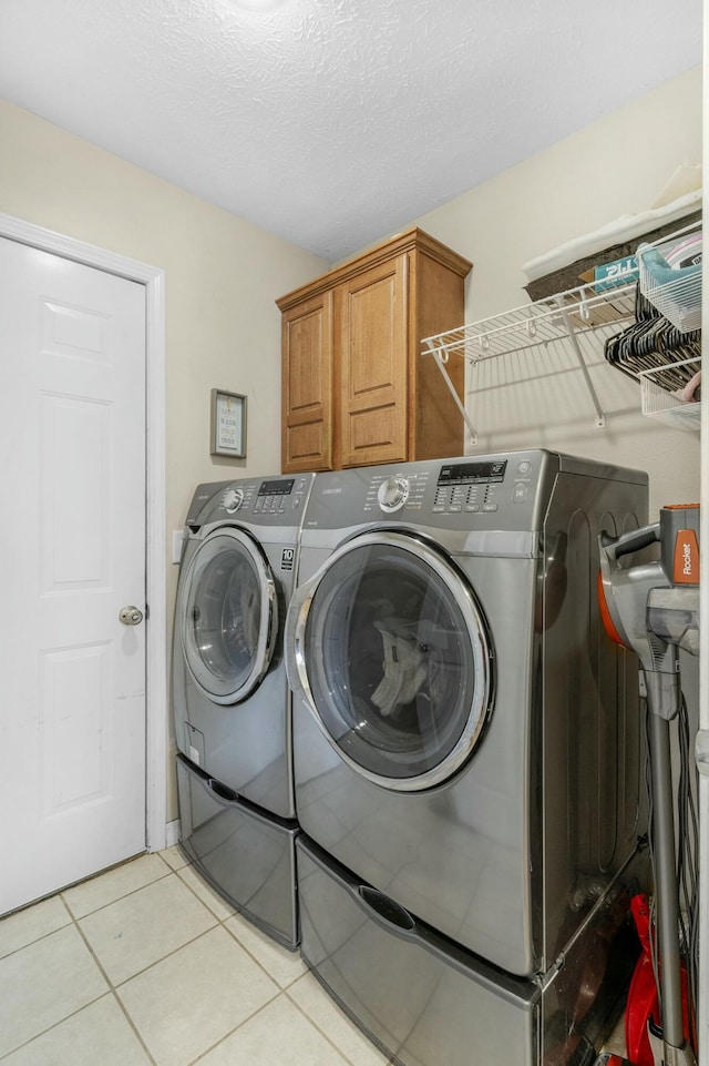 washroom featuring light tile patterned floors, cabinet space, a textured ceiling, and independent washer and dryer