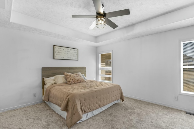 carpeted bedroom featuring baseboards, visible vents, a textured ceiling, and a tray ceiling