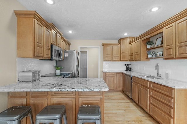 kitchen featuring light stone counters, light wood finished floors, a peninsula, a sink, and appliances with stainless steel finishes