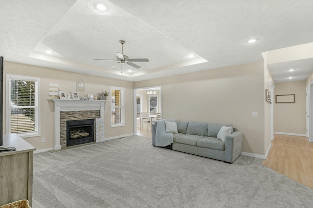 carpeted living room featuring a raised ceiling, recessed lighting, a fireplace, baseboards, and ceiling fan