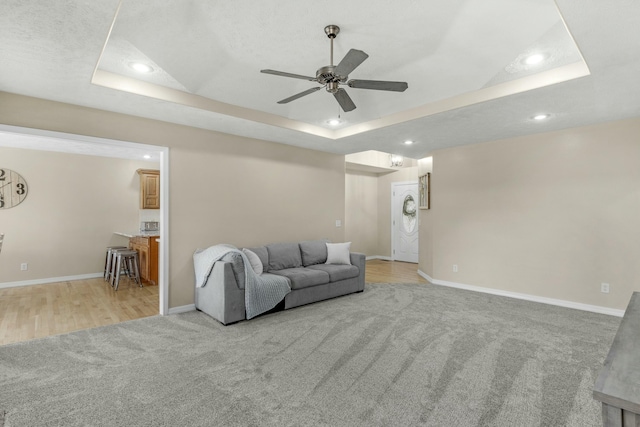 living area with a ceiling fan, baseboards, recessed lighting, a raised ceiling, and light colored carpet