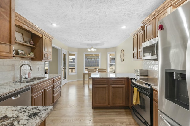 kitchen featuring tasteful backsplash, light stone countertops, light wood-style flooring, appliances with stainless steel finishes, and a peninsula