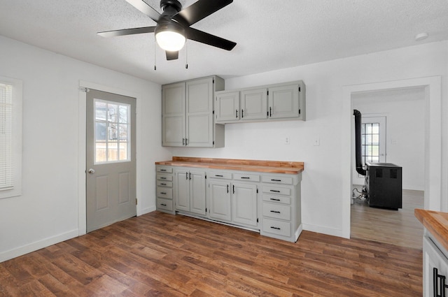 kitchen with wood counters, a textured ceiling, baseboards, ceiling fan, and dark wood-style flooring