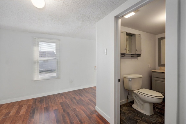 bathroom featuring baseboards, toilet, vanity, wood finished floors, and a textured ceiling