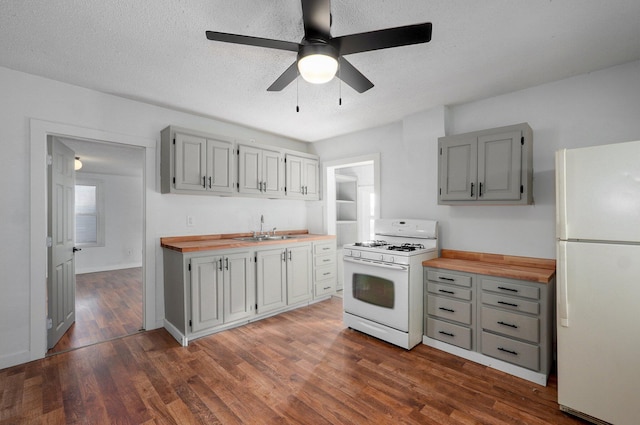 kitchen with white appliances, dark wood finished floors, a sink, gray cabinetry, and wood counters